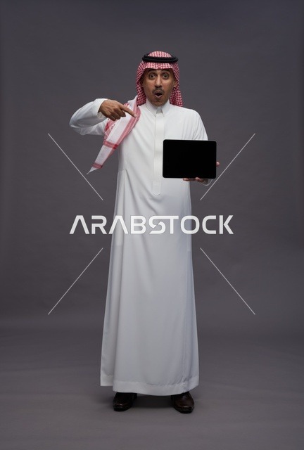 رجل سعودي مندهش يشير إلى جهاز لوحي فارغ