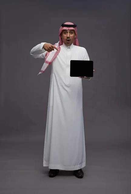 رجل سعودي مندهش يشير إلى جهاز لوحي فارغ