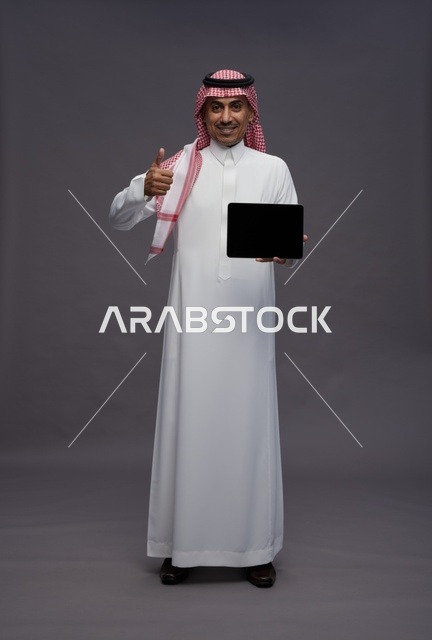 رجل سعودي يمسك جهاز لوحي مع إيماءة الإعجاب