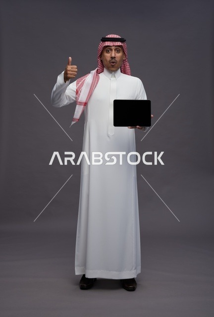 رجل سعودي يحمل جهاز لوحي مع إيماءة الإبهام للأعلى