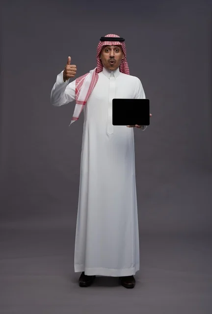 رجل سعودي يحمل جهاز لوحي مع إيماءة الإبهام للأعلى
