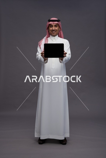 رجل سعودي يمسك جهاز لوحي بشاشة فارغة في استوديو