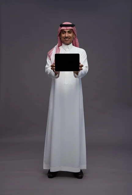 رجل سعودي يمسك جهاز لوحي بشاشة فارغة في استوديو