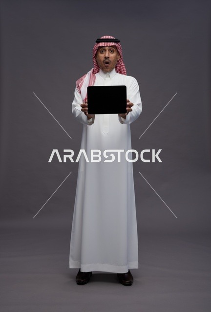 رجل سعودي يمسك بجهاز لوحي بتعبير وجه مندهش