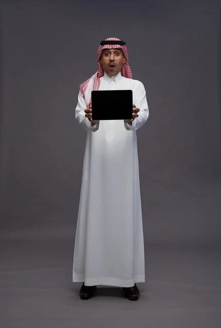 رجل سعودي يمسك بجهاز لوحي بتعبير وجه مندهش