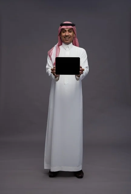 رجل سعودي بالزي التقليدي يحمل جهازاً لوحياً