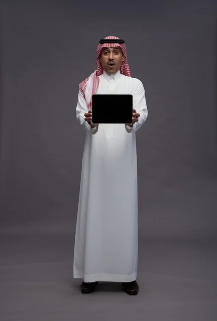 رجل سعودي يمسك بجهاز لوحي بتعبيرات وجه مندهشة