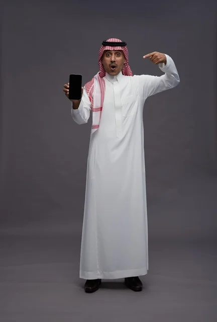 رجل سعودي يشير إلى هاتف ذكي بتعبير مندهش