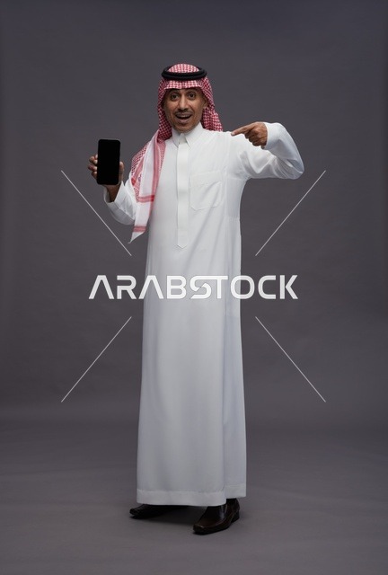 رجل سعودي يحمل هاتف ذكي بتعبير مندهش