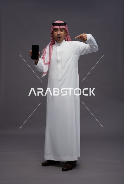 رجل سعودي يشير إلى الهاتف بتعبير وجه مندهش
