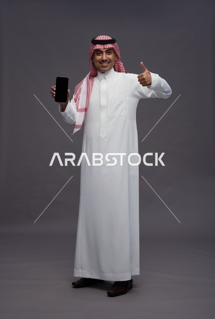 رجل سعودي يمسك هاتف ذكي مع إيماءة الإعجاب