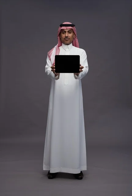 رجل سعودي بالزي التقليدي يحمل جهاز لوحي