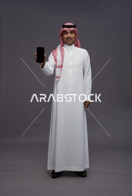 رجل سعودي بالثوب التقليدي يحمل هاتفاً ذكياً