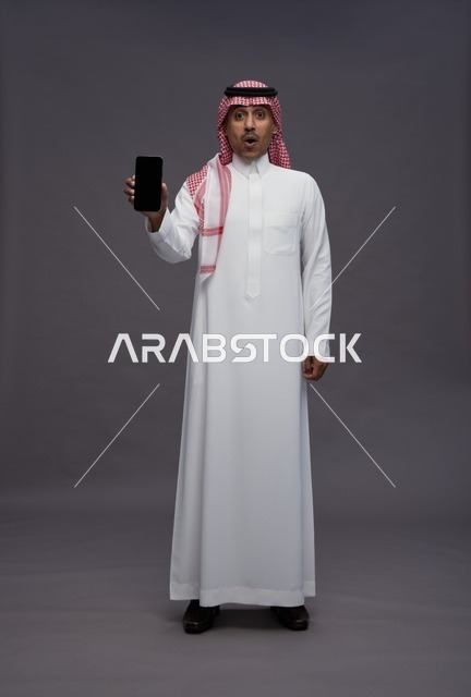 رجل سعودي مندهش يحمل هاتف ذكي بشاشة سوداء أمام الكاميرا