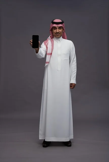 رجل سعودي يحمل هاتف ذكي بشاشة فارغة في الاستوديو