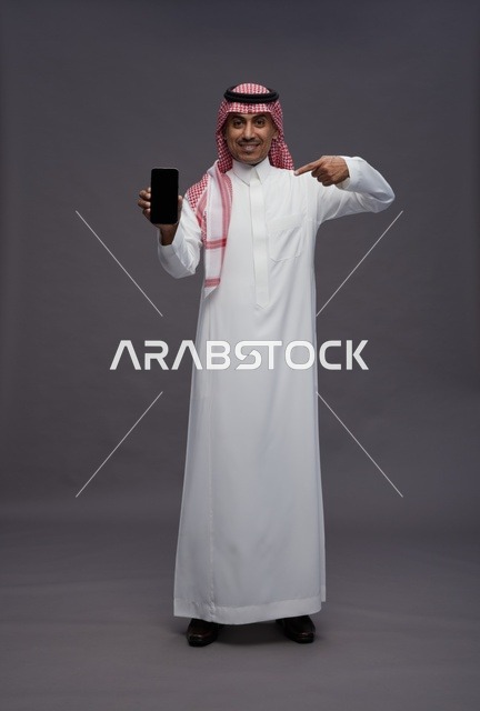 رجل سعودي يحمل هاتف ذكي ويشير إلى الشاشة