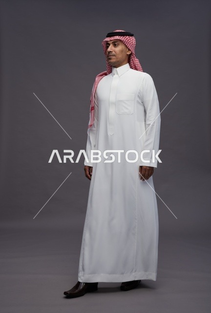 رجل سعودي بالثوب التقليدي والشماغ الأحمر بخلفية رمادية