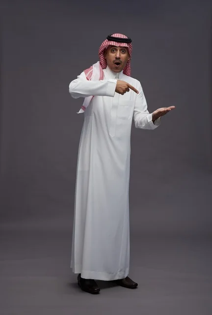 رجل سعودي متفاجئ يشير إلى يده المفتوحة في الاستوديو