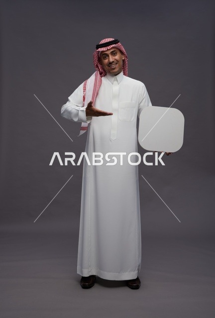 رجل سعودي يحمل لوحة بيضاء فارغة على خلفية رمادية