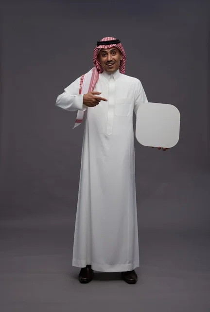 رجل سعودي بالزي التقليدي يشير إلى لوحة بيضاء فارغة