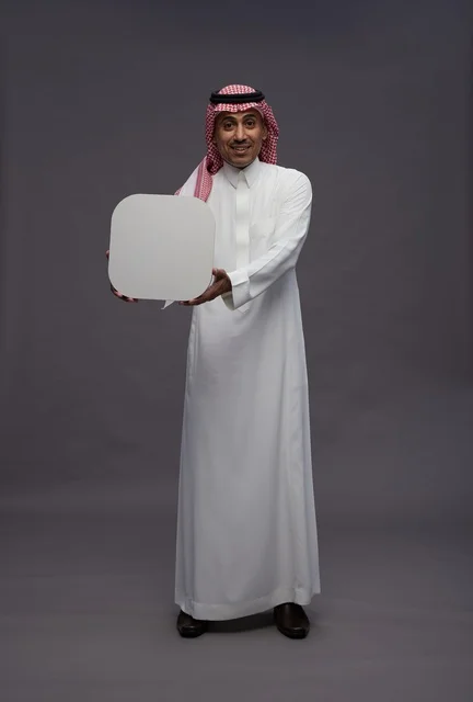 Saudi Man Holding Blank Speech Bubble in Gray Studio