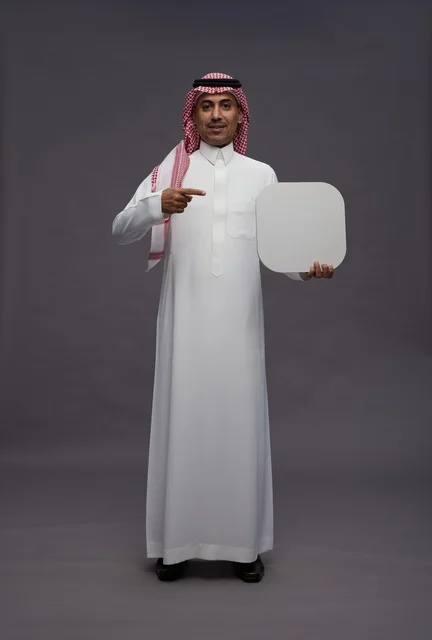 رجل سعودي يحمل لوحة بيضاء فارغة على خلفية رمادية