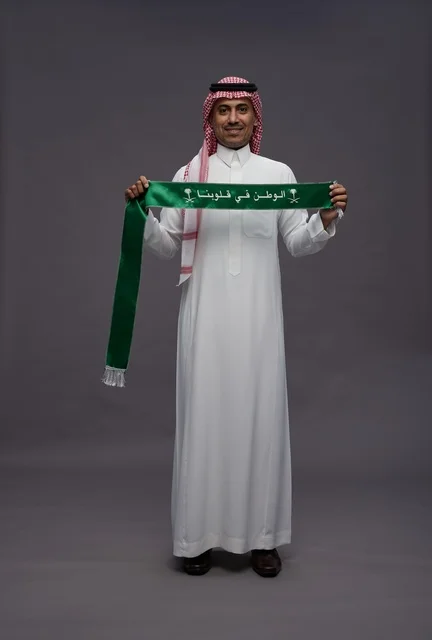 رجل سعودي بالثوب التقليدي يحمل وشاحاً وطنياً