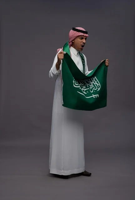 رجل سعودي يحمل العلم الوطني على خلفية رمادية