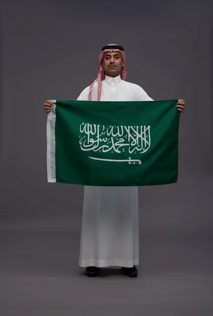 رجل سعودي بالزي التقليدي يحمل علم المملكة العربية السعودية