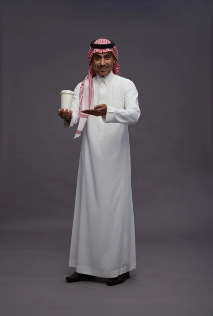 رجل سعودي بالزي التقليدي يحمل كوب قهوة رجل سعودي بالزي التقليدي يحمل كوب قهوة