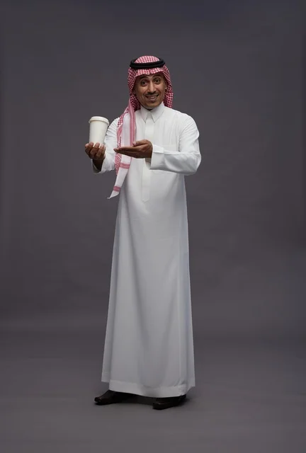 رجل سعودي يرتدي الزي التقليدي يحمل كوب قهوة في استوديو