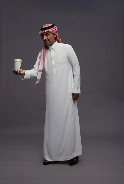 رجل سعودي بالزي التقليدي يحمل كوب قهوة ورقي