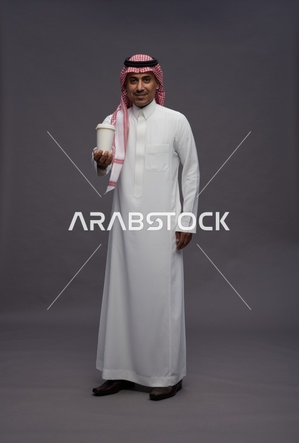 رجل سعودي بالزي التقليدي يحمل كوب قهوة في استوديو