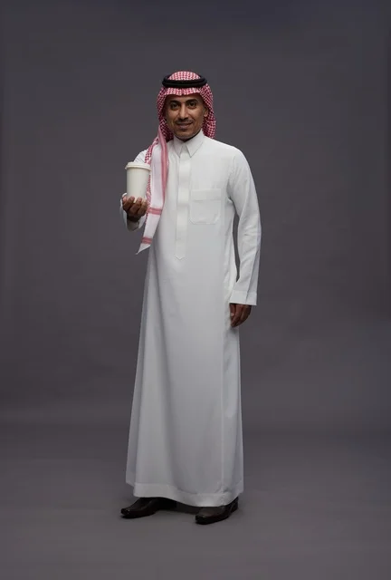 رجل سعودي بالزي التقليدي يحمل كوب قهوة في استوديو