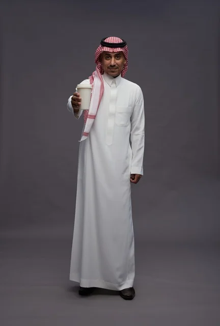 رجل سعودي بالزي التقليدي يحمل كوب قهوة