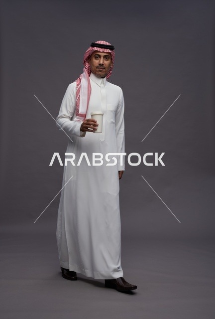 رجل سعودي بالثوب التقليدي يحمل كوب قهوة في الاستوديو