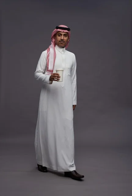 رجل سعودي بالثوب التقليدي يحمل كوب قهوة في الاستوديو