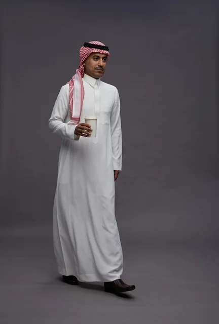 رجل سعودي بالزي التقليدي يحمل كوب قهوة