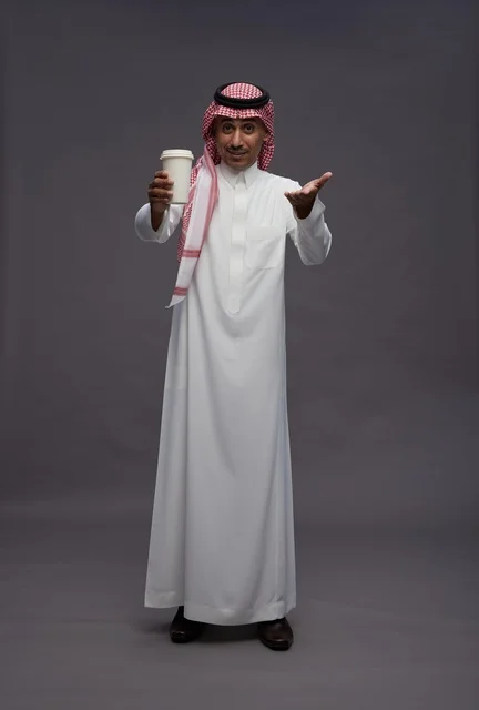 رجل سعودي بالزي التقليدي يحمل كوب قهوة في استوديو