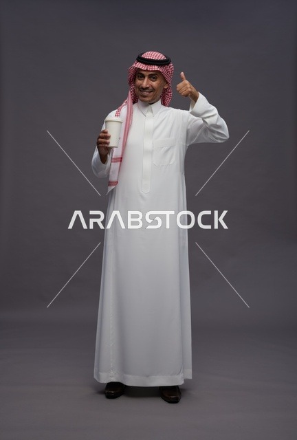 رجل سعودي بالزي التقليدي يحمل كوب قهوة في الاستوديو