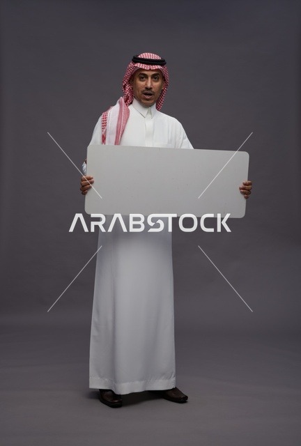 رجل سعودي يحمل لوحة بيضاء فارغة بخلفية رمادية