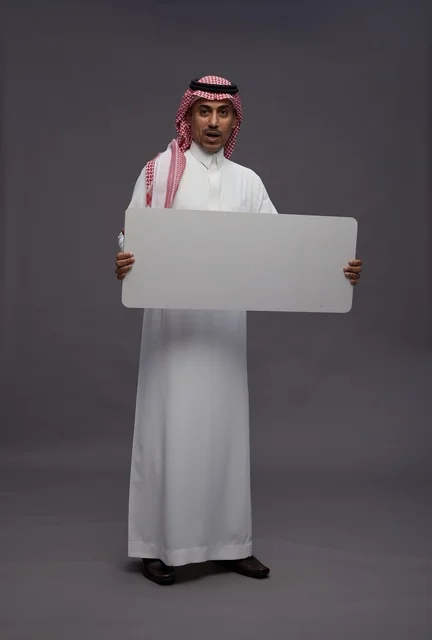 رجل سعودي يحمل لوحة بيضاء فارغة بخلفية رمادية