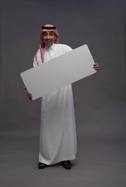 رجل سعودي يحمل لوحة بيضاء فارغة في استوديو