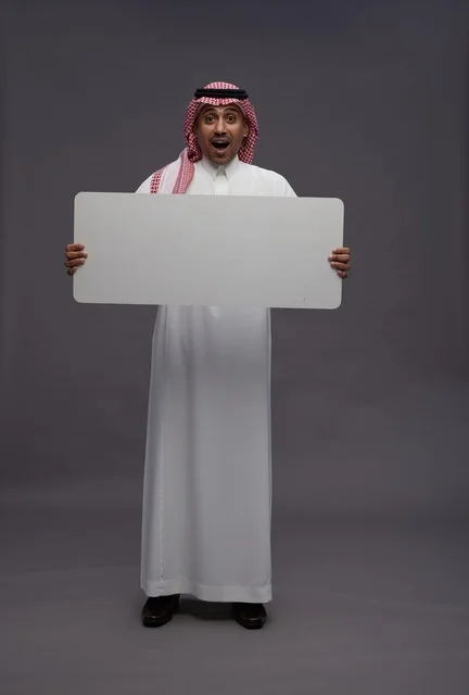 رجل سعودي يحمل لوحة بيضاء فارغة بخلفية رمادية