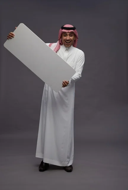رجل سعودي يحمل لوحة بيضاء فارغة في الاستوديو
