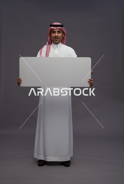 رجل سعودي يحمل لوحة بيضاء فارغة في استوديو