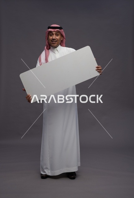 رجل سعودي يحمل لوحة بيضاء فارغة بخلفية رمادية