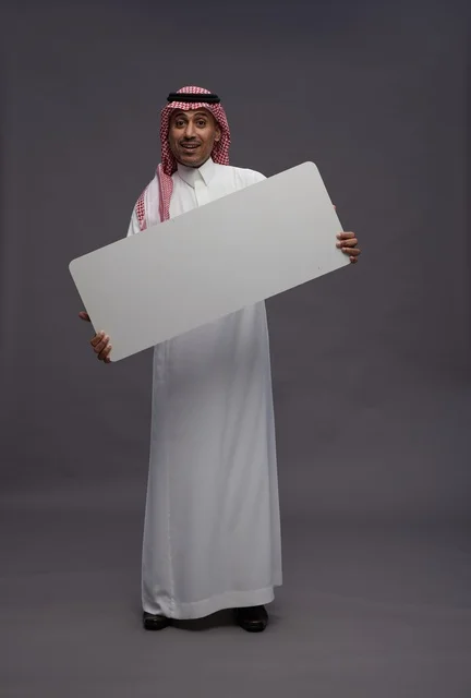 رجل سعودي يحمل لوحة بيضاء فارغة بخلفية رمادية رجل سعودي يحمل لوحة بيضاء فارغة بخلفية رمادية