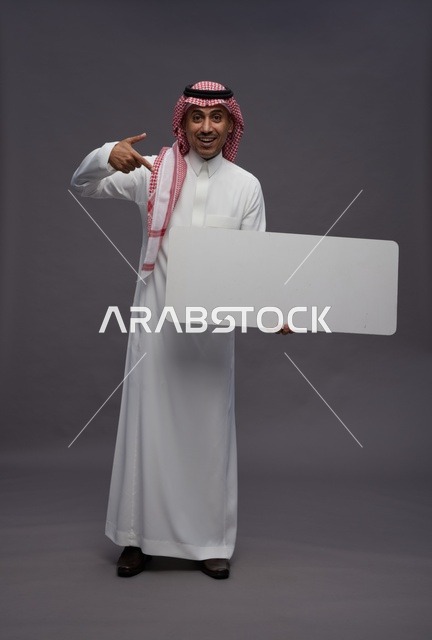 رجل سعودي يحمل لوحة بيضاء فارغة أمام خلفية رمادية