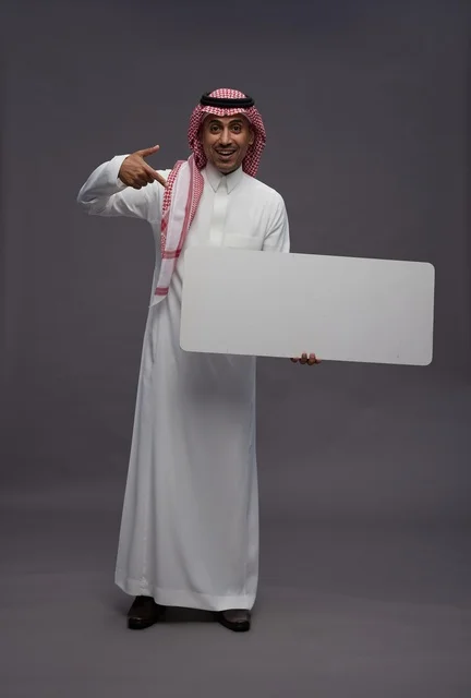 رجل سعودي يحمل لوحة بيضاء فارغة أمام خلفية رمادية
